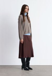 Brauner Midirock, grauer gestrickter Pullover, hellblaues Rollkragenoberteil und schwarze strukturierte kniehohe Stiefel. Schlichte, lockere Passform mit weichen Texturen.