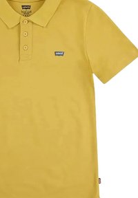 Polo giallo realizzato in cotone con colletto, tre bottoni e un piccolo logo blu di Levi's sul petto. Texture liscia; maniche corte.