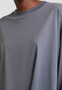 Mand iført en enkel, løsgribende grå t-shirt med rund hals, der er cropped for kun at vise hals og overkrop.