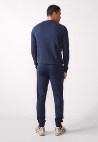 Navy blue sweatshirt and joggers in soft fabric, featuring ribbed cuffs and a back pocket. Footwear has gray and yellow accents.