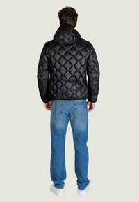 Czarna puchowa kurtka z kapturem i wzorem w romby, w połączeniu z jasnoniebieskimi dżinsami i białymi trampkami. Widok od tyłu.