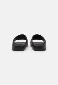 Black sandals with open backs, made of lightweight material. Features a smooth texture, flat soles, and simple, minimalist design.