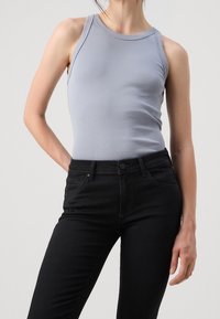 Ljust grå ärmlös topp i kombination med svarta tajta jeans, med en slät textur och minimalistisk design, utan mönster eller utsmyckningar.