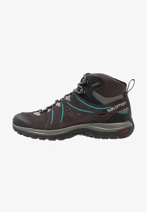 Botte de randonnée mi-haute gris foncé avec des accents bleu sarcelle, lacets à l'avant, semelle texturée et marquage Salomon sur le côté et la boucle au talon.
