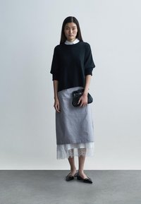 Sort strikket trøje, gråt lagdelt skørt med blonderkant og en lille sort håndtaske. Flade sorte sko fuldender outfittet. Minimalistisk design.