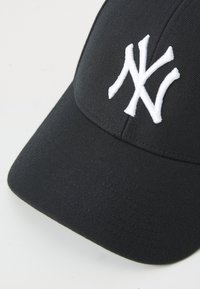 Sort baseballcap lavet af stof, med et hvidt broderet "NY" logo foran, struktureret form og en buet skygge.