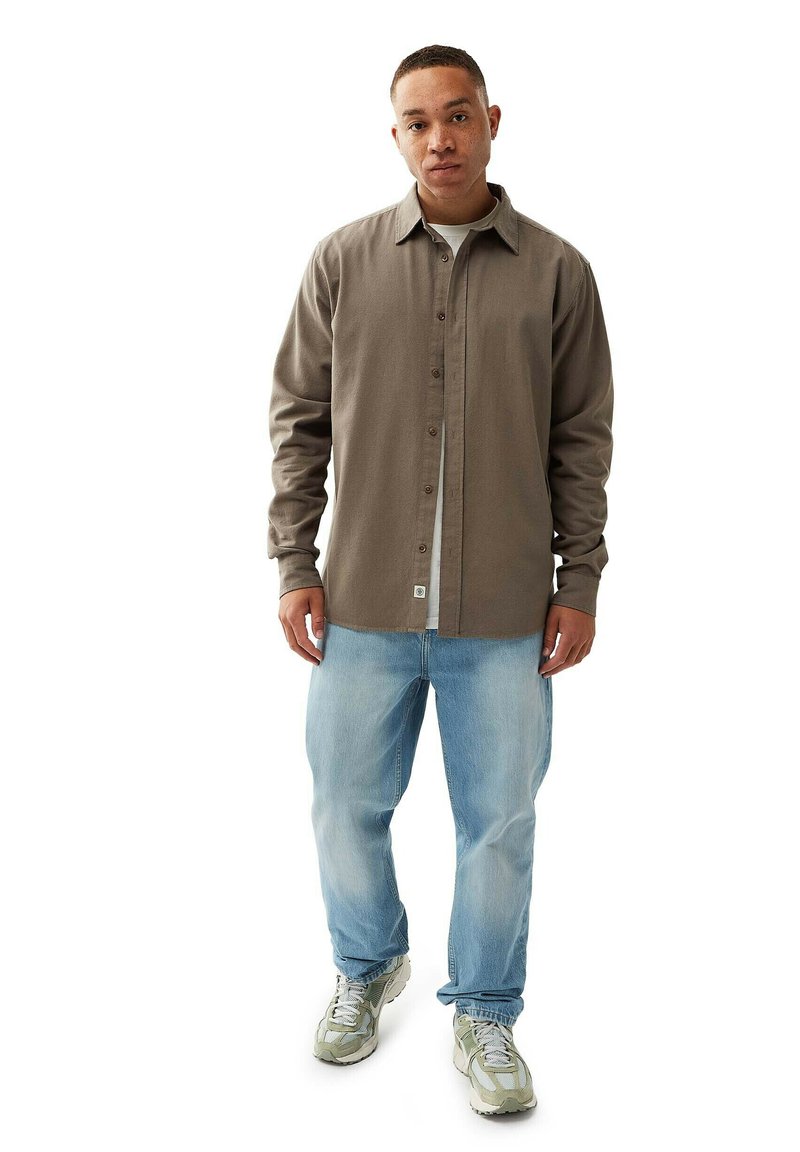Brun button-up skjorte med krave, parret med lyseblå denim jeans og grå sneakers med et struktureret design.
