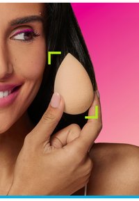 Beige make-up spons in een druppelvorm, vasthouden tussen de vingers; huidachtige textuur; achtergrondverloop van roze naar paars.