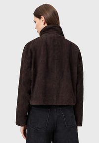 Giacca in camoscio marrone con collo alto, design corto e vestibilità comoda. Presenta spalle scese e dettagli senza cuciture sul retro.