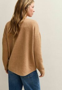 Camelkleurige gebreide trui met een losse pasvorm, verlaagde schouders en geribde manchetten. Beschikt over een iets langere achterkant en een zachte textuur.