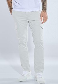 Hellgraue Cargo-Hosen mit seitlichen Taschen, im geraden Schnitt, aus einem Baumwollgemisch, kombiniert mit weißen Turnschuhen.