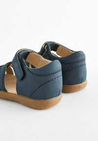 Blaue Wildledersandalen mit offenem Design, verstellbaren Klettverschlüssen, weichem, tanfarbenem Lederfutter und braunen Gummisohlen. Verstärkte Nahtdetails.