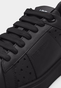 Μαύρο δερμάτινο αθλητικό παπούτσι με μαύρα κορδόνια, διάτρητα σχήματα καρδιάς στα πλάγια και ανάγλυφο λογότυπο "LOVE MOSCHINO" στην εξωτερική πλευρά.