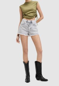 Top corto verde oliva con fruncidos laterales, combinado con pantalones cortos de mezclilla claros con bordes deshilachados. Botas de vaquero de cuero negro con diseño embosado.
