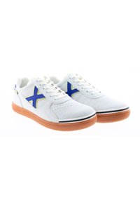 Zapatillas deportivas blancas con acentos azules y un diseño perforado. Sus características incluyen una puntera redondeada, suela texturizada y un contorno amarillo en el logotipo.
