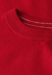 Tessuto di un maglione rosso lavorato a maglia con scollatura a girocollo a costine. Presenta righe bianche attorno al collo, con una finitura morbida e texture.