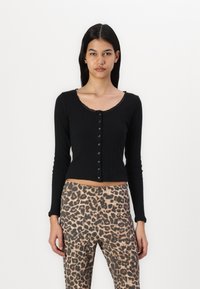Crna rebrasta majica dugih rukava s izrezanim dekolteom, zatvaranjem na gumbe i dekorativnim rubom; u kombinaciji s hlačama s leopard uzorkom visokog struka.