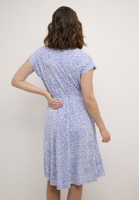 Blaue gemusterte Kleid mit kurzen Ärmeln, das einen gerafften Rücken, einen fließenden Rock und eine leichte Stofftextur aufweist.