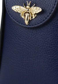 Donkerblauwe leren handtas met een getextureerde afwerking, afgewerkt met een decoratieve gouden bijenbroche voor extra detail.