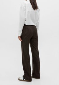 Bruna randiga byxor med rak skärning, med en mid-rise midja och tygtextur. I kombination med en vit långärmad skjorta och sneakers.