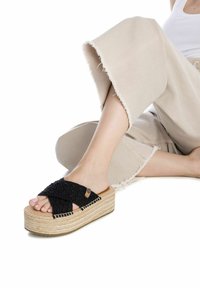 Sandalias plataformas trenzadas negras con suela de yute. La parte superior cuenta con un diseño de tiras en forma de X y un pequeño logotipo en el costado.
