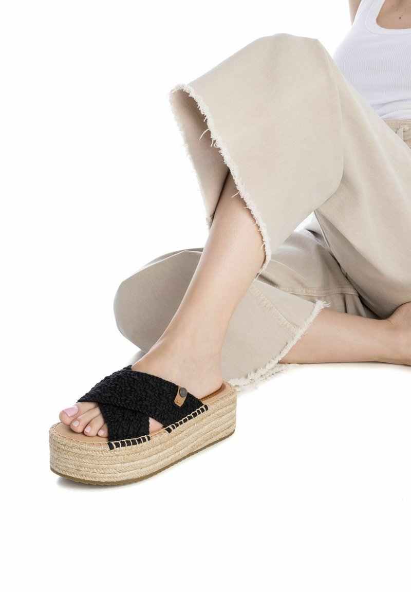 Sandalias plataformas trenzadas negras con suela de yute. La parte superior cuenta con un diseño de tiras en forma de X y un pequeño logotipo en el costado.