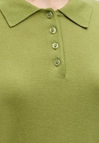 Polo en maille vert avec un col pointu et quatre boutons verts translucides sur la patte de boutonnage avant.