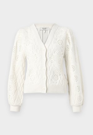 Balts adīts cimdiņš ar V veida kakla izgriezumu, pogu aizdari un smalkām acu detaļām. Puffētas piedurknes un ribota apakšmala pievieno struktūru.