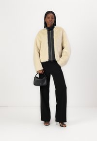 Giacca in finta pelliccia crema sopra un top in pelle nera, abbinata a pantaloni larghi neri e una borsa nera. Sandali neri con tacchi a strappo completano il look.