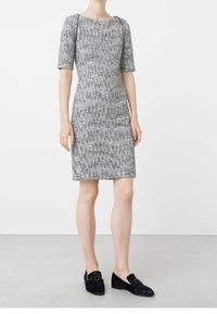 Harmaa ja valkoinen teksturoitu polvipituinen mekko, jossa on lyhyet hihat ja pyöreä pääntie, yhdistettynä mustiin loafer-kengiin, joissa on koristeellisia metalliosia.