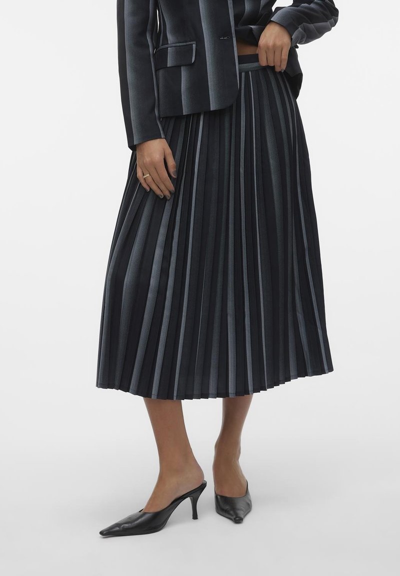 Jupe midi plissée bleu marine foncé avec des rayures gris clair, en tissu texturé. Associée à des mules noires à talons pointues.