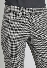 Svart- och vitrutigt mönstrade byxor i hounds-tooth, med en mjuk textur, slim fit, midjehöjd och diskreta framfickor.