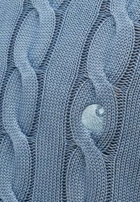 Ανοιχτό μπλε πλεκτό ύφασμα με σχέδιο πλέξης καλωδίου, που περιλαμβάνει ανυψωμένες στριφογυριστές περιοχές και μια ομαλή κυκλική πλεκτή λεπτομέρεια μέσα στο σχέδιο.