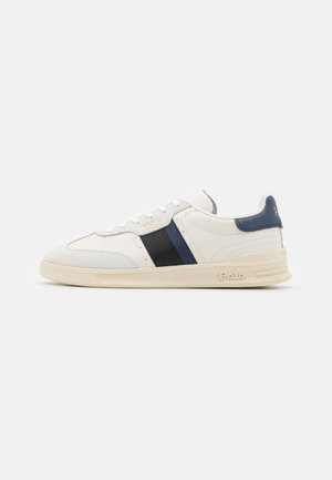 Białe niskie sneakersy z granatowo-czarnymi paskami po bokach, logo Polo na boku i pięcie, beżową podeszwą i białymi sznurowadłami.