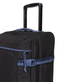 Valigia nera in tessuto con manico estraibile, dettagli blu, tasca con zip e una cinghia con fibbia per fissare il contenuto.