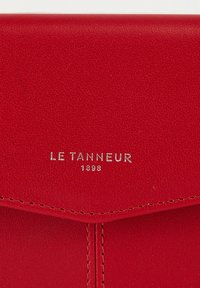 Portafoglio in pelle rossa con finitura testurizzata, caratterizzato dal logo argento "LE TANNEUR 1898". Le linee pulite e il design piegato esaltano la sua forma.