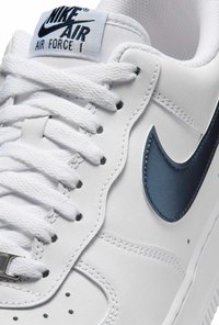 Witte Nike Air Force 1 sneaker met marineblauwe swoosh en "Nike Air" logo op de tong, voorzien van witte veters en gedetailleerde stiksels.