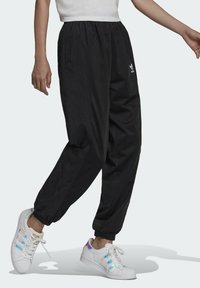 Svarta lätta träningsbyxor med elastisk midja, med sidfickor och en liten vit Adidas-logotyp på vänster lår.