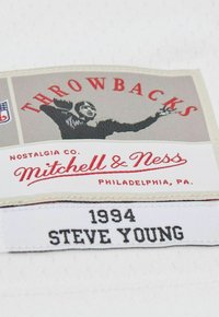 Vintage sports label with a player catching a football, "THROWBACKS" text, Mitchell & Ness logo, and "1994 STEVE YOUNG" printed below.