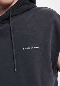 Svart ermeløs hettegenser med teksturert finish. Har et hvitt "NINETEEN NINETY"-logo på fronten.