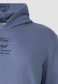 Felpa blu chiaro con una texture morbida; presenta una stampa frontale con un logo di un cavallo e il testo "Ford Bronco Dal 1966."