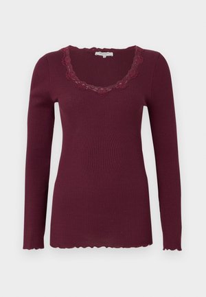 Burgundowy longsleeve z prążkowanej tkaniny, z falbaniastym koronkowym dekoltem i dołem, wykonany z miękkiego, elastycznego materiału.
