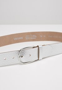 Ceinture en cuir argenté avec une finition texturée, dotée d'une boucle en métal argenté et de trous pour le réglage. L'intérieur est beige avec des détails de branding.