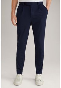 Marineblaue, maßgeschneiderte Hosen aus glattem Stoff, mit seitlichen Taschen, flachem Frontdesign und schmaler Passform, kombiniert mit weißen Sneakers.