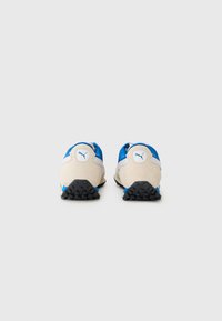Scarpe sportive con tomaia in suede beige e mesh blu, suola in gomma nera e piccoli tacchetti per la trazione. Logo blu sul tallone.