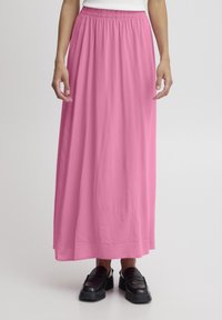 Larga falda rosa con una cintura elástica, que cae holgadamente para un ajuste relajado. Presenta una textura suave y se acompaña de zapatos de plataforma negros.