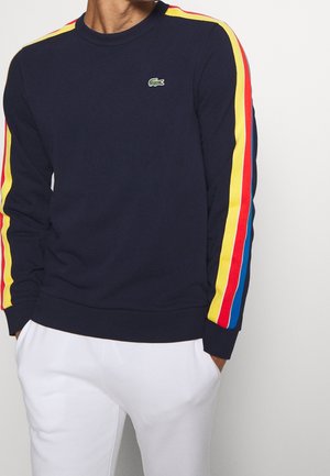 Marine sweatshirt met rode, gele en blauwe strepen op de mouwen; ribgebreide manchetten en zoom; Lacoste-logo op de borst. Zachte stofstructuur.