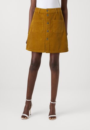 A corduroy mini skirt in mustard yellow with a fitted waist, two front pockets, and a button closure down the center. Textured design.