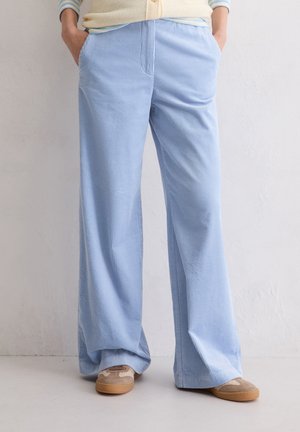 Hellblaue, weite Cordhosen mit vertikalen Streifen, ausgestattet mit vorderen Taschen und einem lockeren Schnitt, kombiniert mit beigen Slippern.