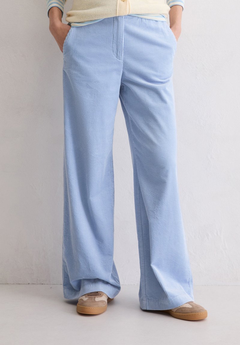 Hellblaue, weite Cordhosen mit vertikalen Streifen, ausgestattet mit vorderen Taschen und einem lockeren Schnitt, kombiniert mit beigen Slippern.